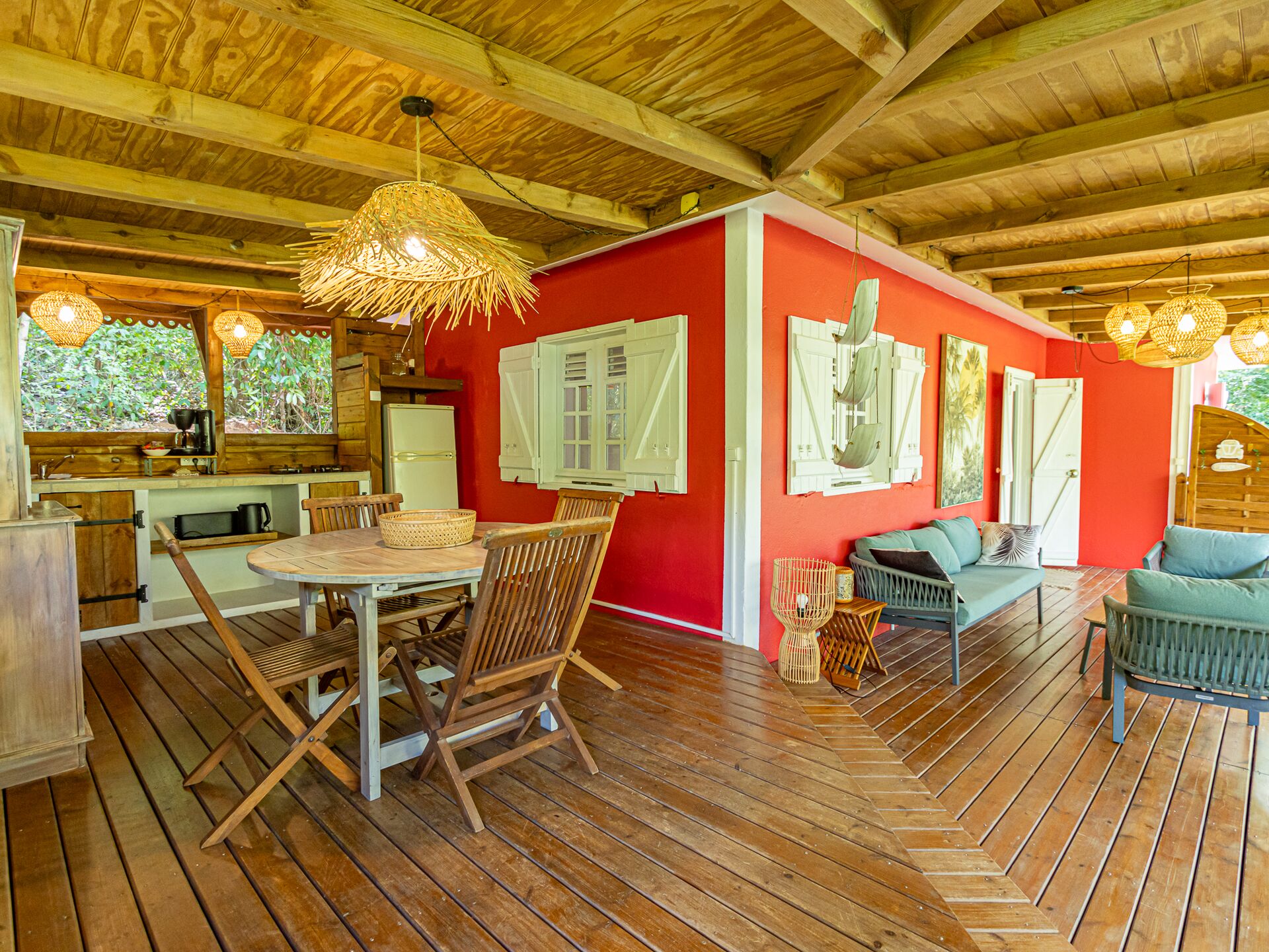 Vue de la terrasse extérieure avec la cuisine équipée, une table et quatre chaises ainsi qu'un canapé dans la villa Kariakou du Caraïb'Bay Hôtel